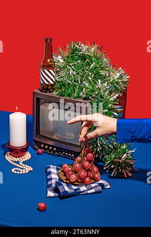 Angolo alto di serie televisiva vintage circondato da una serie di oggetti diversi su un tavolo blu su sfondo rosso, mentre una persona anonima ritagliata p Foto Stock
