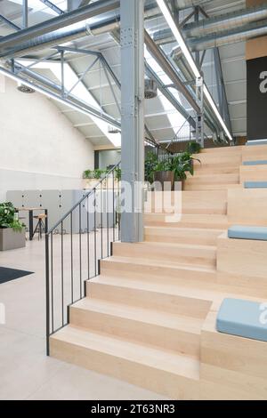 Moderno ufficio di coworking a Madrid in Spagna che presenta un'area salotto in legno a più livelli con cuscini blu travi metalliche e pareti bianche illuminate Foto Stock