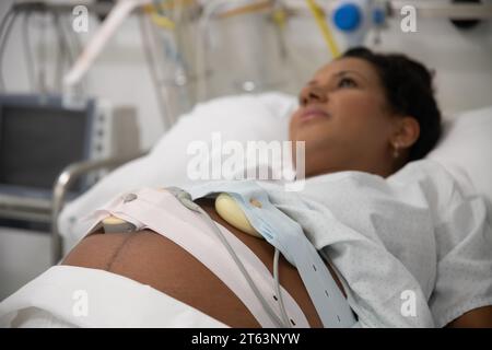 Donna incinta che riposa in un letto d'ospedale, apparecchiature di monitoraggio in background Foto Stock