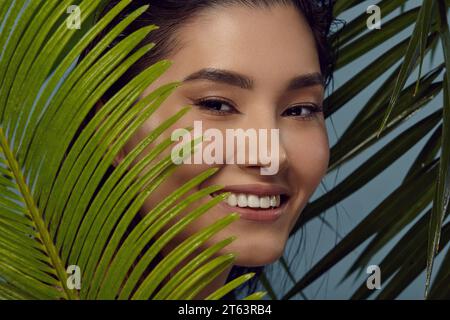 Ragazza giocosa si sbircia da dietro le foglie di palma, sorride. Foto Stock
