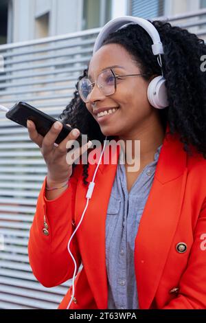 Donna afro-americana felice che utilizza il riconoscimento vocale su smartphone all'aperto. Foto Stock
