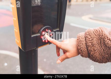 donna che attraversa la strada e preme il pulsante del semaforo Foto Stock