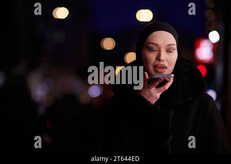 Donna d'affari musulmana Hijabi che controlla il suo telefono sulla strada urbana di notte Foto Stock