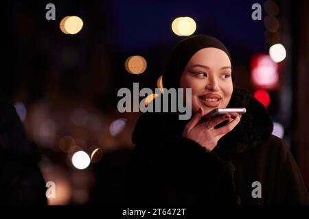 Donna d'affari musulmana Hijabi che controlla il suo telefono sulla strada urbana di notte Foto Stock