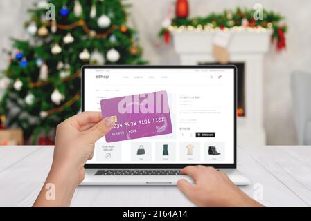 Shopping natalizio online su computer portatile con carta di credito. Albero di Natale e camino sullo sfondo Foto Stock