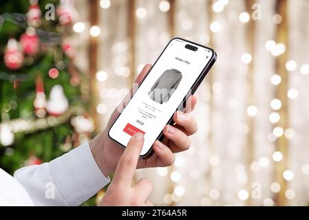 Shopping natalizio tramite cellulare sul moderno sito di e-commerce. Luci dell'albero di Natale e bokeh sullo sfondo Foto Stock