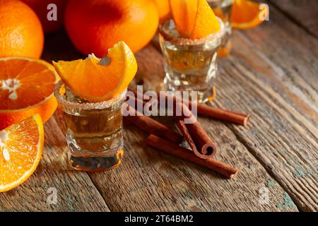 Bicchieri di liquore all'arancia guarniti con zucchero e cannella in polvere. Liquore all'arancia con frutta fresca su un vecchio tavolo di legno. Foto Stock