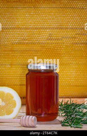 Un barattolo di miele, dispenser, rametto di rosmarino e mezzo limone su legno con un vero favo a nido d'ape sullo sfondo. Spazio per il testo Foto Stock