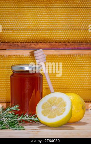 Dispenser poggiato su un vaso di miele, un rametto di rosmarino e un limone e mezzo su legno con un vero favo sullo sfondo. Spazio per il testo Foto Stock