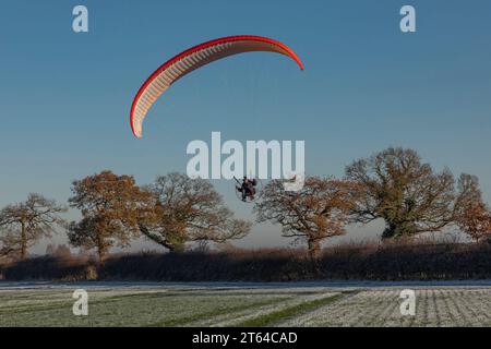 Campo verde coperto di ghiaccio con parapendio che arriva a terra con una vela arancione Foto Stock