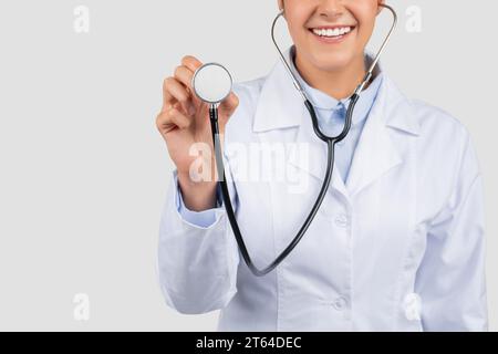 Sorridente medico millenario europeo in camice bianco, ascolta respirare con stetoscopio, tagliato Foto Stock