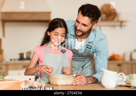 Ragazza che si rompe l'uovo con l'aiuto di papa' Foto Stock