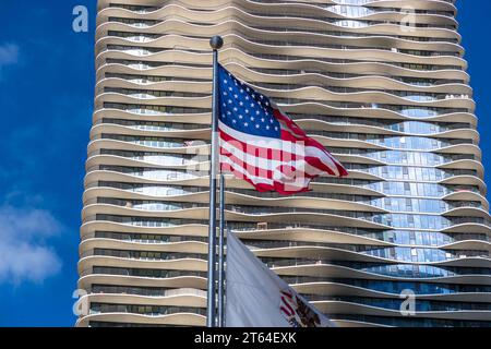 Una bandiera americana sventola davanti alla facciata a forma d'onda dell'Aqua Tower a Chicago, Illinois, Stati Uniti. Il grattacielo pluripremiato di 81 piani con i suoi balconi ondulati e fluenti è stato progettato dall'architetto Jeanne Gang dello Studio Gang Architects ed è stato nominato, tra gli altri riconoscimenti, Grattacielo dell'Anno. Foto Stock