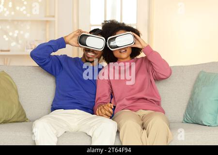 Coniugi afroamericani che indossano cuffie per realtà virtuale in salotto Foto Stock