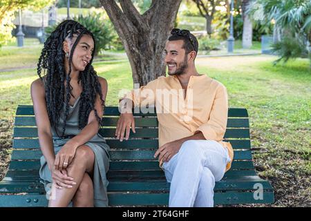 Tre giovani adulti allegri, un gruppo eterogeneo, che ridono e si godono una giornata di sole su una panchina del parco. Foto Stock