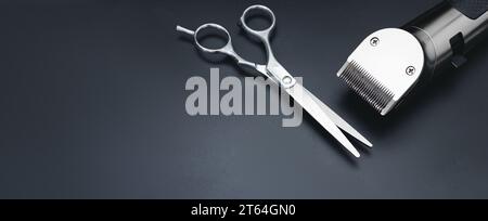 Regolacapelli e forbici da parrucchiere su sfondo nero. Scrivania per parrucchiere uomo con strumenti per la rasatura in alto. Taglio di capelli maschile, moda. Parrucchiere Foto Stock