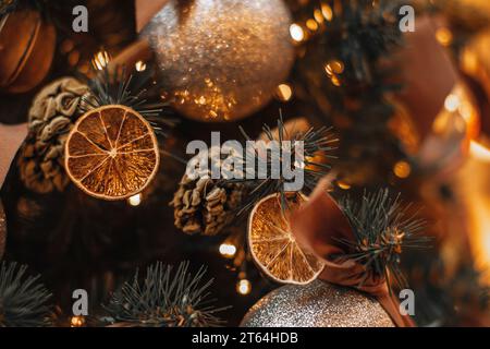 Decorazioni magiche invernali. Rami dell'albero di Natale decorati con arance secche, mandarini e coni di pino. Dettagli creativi e accoglienti e bokeh garla dorata Foto Stock