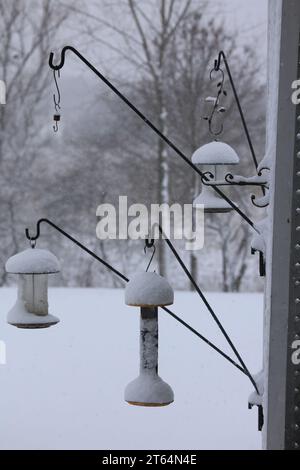 Tre mangiatoie appese a ganci di ferro nero, attaccati a un traliccio di legno, ricoperti di diversi centimetri di neve durante una tempesta di neve nel Wisconsin Foto Stock