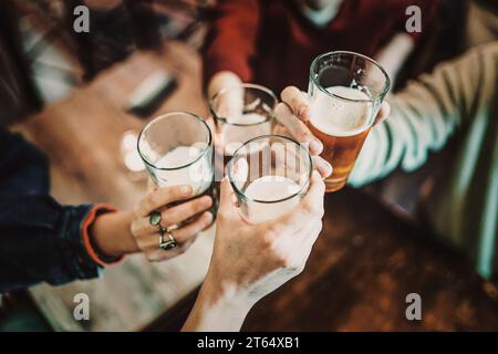 Primo piano di un allegro gruppo di amici che brinda con bicchieri di birra e latte, godendosi un momento di socializzazione insieme. Foto Stock