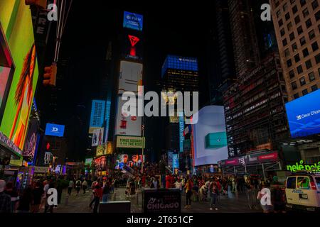 I grattacieli di Manhattan prendono vita di notte, con i vivaci cartelloni a LED che illuminano Broadway e la folla di persone che si aggirano intorno alle iconiche scale rosse i. Foto Stock