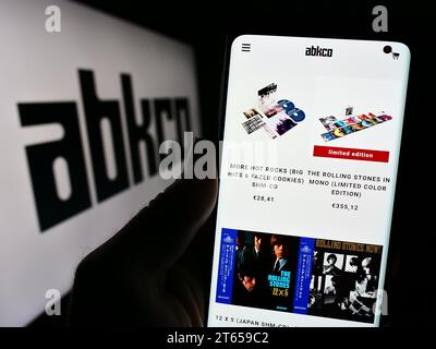 Persona che possiede un telefono cellulare con il sito Web della casa discografica statunitense ABKCO Music Records Inc. Davanti al logo. Concentrarsi sul centro del display del telefono. Foto Stock