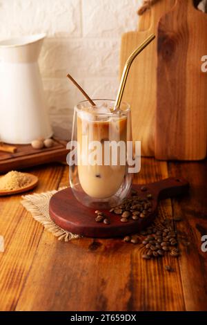 Caffè freddo servito in una tazza di vetro a doppia parete e paglia di metallo, una bevanda estiva fredda preparata con cubetti di ghiaccio e spezie, cannella, noce moscata, vaniglia, mu Foto Stock