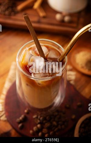 Caffè freddo servito in una tazza di vetro a doppia parete e paglia di metallo, una bevanda estiva fredda preparata con cubetti di ghiaccio e spezie, cannella, noce moscata, vaniglia, mu Foto Stock