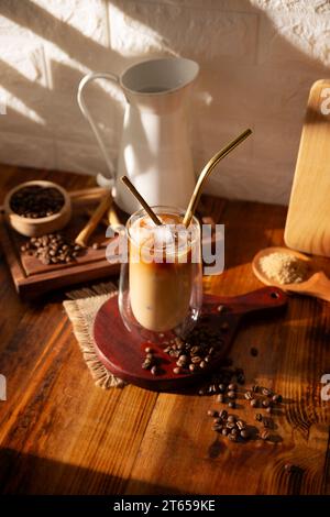 Caffè freddo servito in una tazza di vetro a doppia parete e paglia di metallo, una bevanda estiva fredda preparata con cubetti di ghiaccio e spezie, cannella, noce moscata, vaniglia, mu Foto Stock