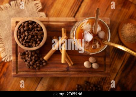 Caffè freddo servito in una tazza di vetro a doppia parete e paglia di metallo, una bevanda estiva fredda preparata con cubetti di ghiaccio e spezie, cannella, noce moscata, vaniglia, mu Foto Stock