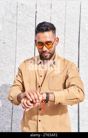 ritratto di un uomo latino con occhiali da sole che guardano l'orologio Foto Stock