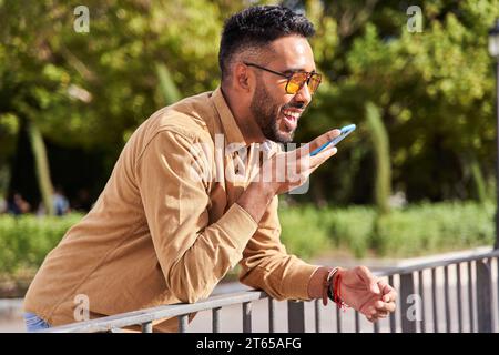 uomo latino con occhiali da sole che invia un messaggio audio tramite uno smartphone. Foto Stock