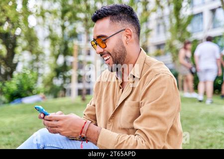 Uomo latino che tiene in mano e usa lo smartphone al parco guardando la cella leggendo nuovi messaggi da cellulare Foto Stock