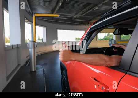 La mano di un uomo con il pollice in alto vicino all'auto quando entra in un parcheggio sotterraneo. Sistema di sicurezza del parcheggio Foto Stock