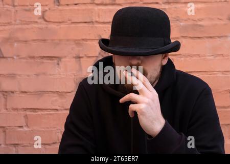 Un uomo nero fuma una sigaretta su uno sfondo da muro. Foto Stock