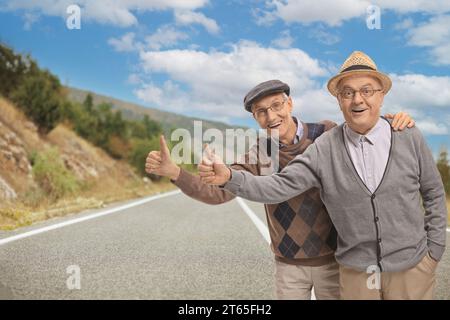 Uomini anziani allegri che fanno autostop su una strada aperta Foto Stock