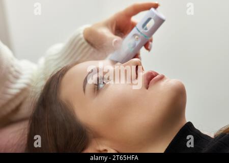 cosmetologo che utilizza primer spray per la procedura di estensione delle ciglia in salone Foto Stock