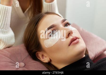 cosmetologo che applica strisce di cotone con colla sotto gli occhi. Procedura di estensione ciglia Foto Stock