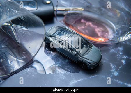 concetto che mostra la guida in stato di ebbrezza. Un'auto giocattolo accanto agli occhiali da alcol. Dipendenza da alcol e pericolo stradale Foto Stock