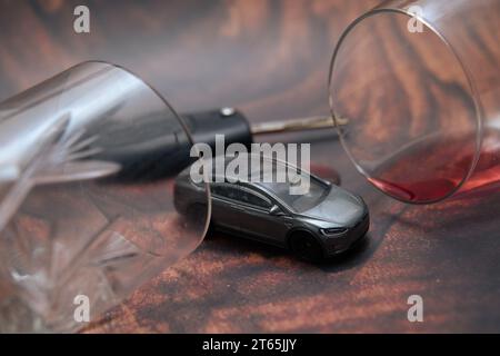 concetto che mostra la guida in stato di ebbrezza. Un'auto giocattolo accanto agli occhiali da alcol. Dipendenza da alcol e pericolo stradale Foto Stock