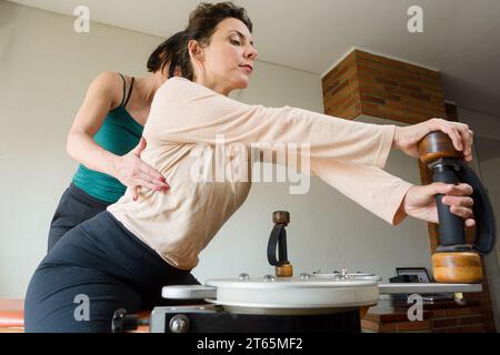 Istruttore caucasico di riabilitazione adulto che corregge la postura posteriore della sua studentessa durante l'allenamento seduta sulla macchina ginnastica gyrotonic, copia sp Foto Stock