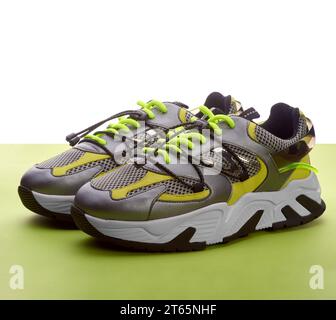 Scarpe da running femminili alla moda grigio metallizzato con lacci verdi brillanti e dettagli gialli e argento su sfondo bianco e verde. Co. Pubblicitaria Foto Stock