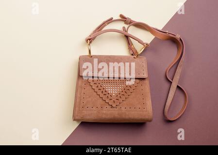 Elegante borsa da donna in pelle scamosciata marrone con spalline e decorazioni traforate originali, su un interessante sfondo bicolore con spazio per la copia Foto Stock