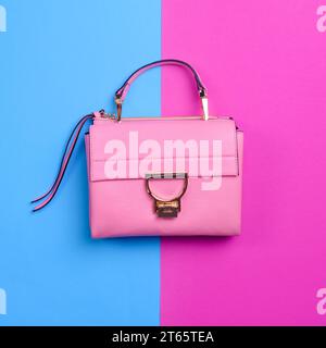 Elegante borsa da donna in pelle rosa con finiture nere, dettagli in metallo dorato, manico superiore e cerniera isolata su uno sfondo blu vivace e fucsia. Foto Stock