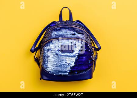 Elegante zaino da donna blu con zip, rivestito di paillettes lucide e isolato su sfondo giallo. Mockup creativo per pubblicizzare una borsa st Foto Stock