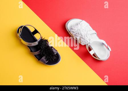 Due eleganti sandali da donna dallo stesso design ma con colori diversi su sfondo giallo-rosso a contrasto. Vista dall'alto, base piatta. Design creativo per la scarpa S. Foto Stock