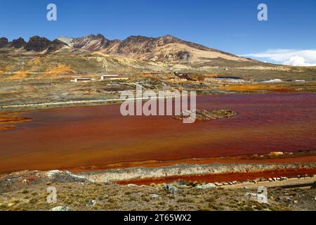 Ammira il lago e l'acquedotto contaminati dal drenaggio delle miniere di acidi e dai rifiuti industriali dalla vicina miniera di stagno di Milluni (parte della quale può essere vista sulla riva e sul fianco della montagna), vicino a la Paz, Bolivia. Le montagne sono ai piedi del massiccio del Monte Chacaltaya. Foto Stock