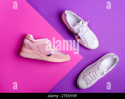 Tre sneaker moderne da donna nei colori bianco e cipria con dettagli alla moda su uno sfondo rosa e viola. Vista dall'alto, base piatta. Creat Foto Stock