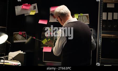 Il detective senior analizza il Consiglio degli indizi nella sala prove, guardando il rapporto forense e le foto di sorveglianza per scoprire l'identità degli assassini. Investigatore privato che spera di fare una scoperta. Scatto manuale. Foto Stock
