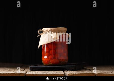 Pomodori ciliegini sottaceto in vasetti di vetro con coperchi artigianali su fondo di legno da vicino, spazio per le copie. Foto Stock