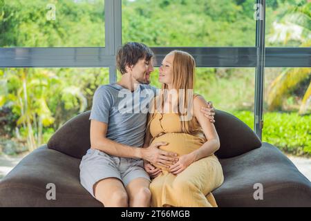 Un momento tenero catturato mentre un marito e una moglie incinta si siedono sul divano, condividendo un abbraccio affettuoso, il loro amore e la loro anticipazione si irradiano nel loro Foto Stock